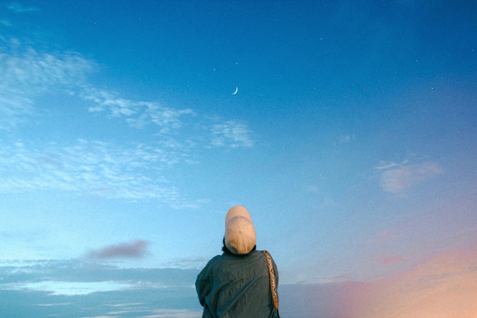 A person gazing up at a crescent moon in a vast dusk sky